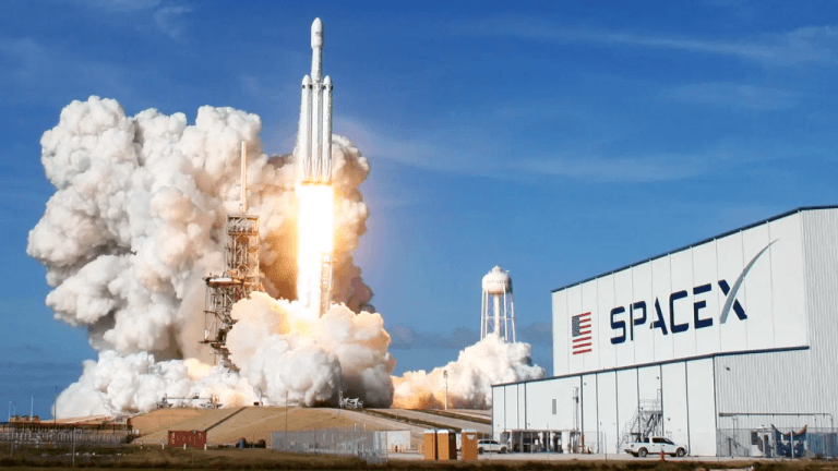 A SpaceX rocket roars off the launch pad as towering clouds of exhaust billow across the launch site.